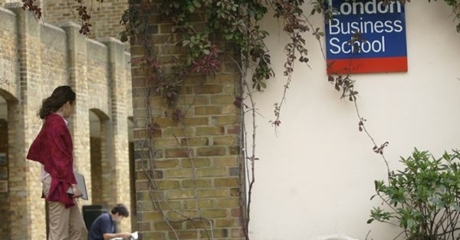 Girl in maroon jacket standing to the left of a wall with a vine growing up next to a sign that says, "London Business School."