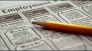 Help Wanted advertizments in a newspaper, listing jobs. A yellow pencil rests on the newspaper.