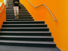 Young woman walking down orange stairs, reading book. Stanford GSB first year advice