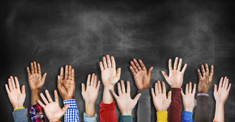 A group of diverse hands raised in front of a recently erased chalkboard.
