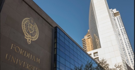 Outside view of building that reads, "Fordham University" in gold lettering. The Fordham Seal is above, also in gold. Tall buildings in background.